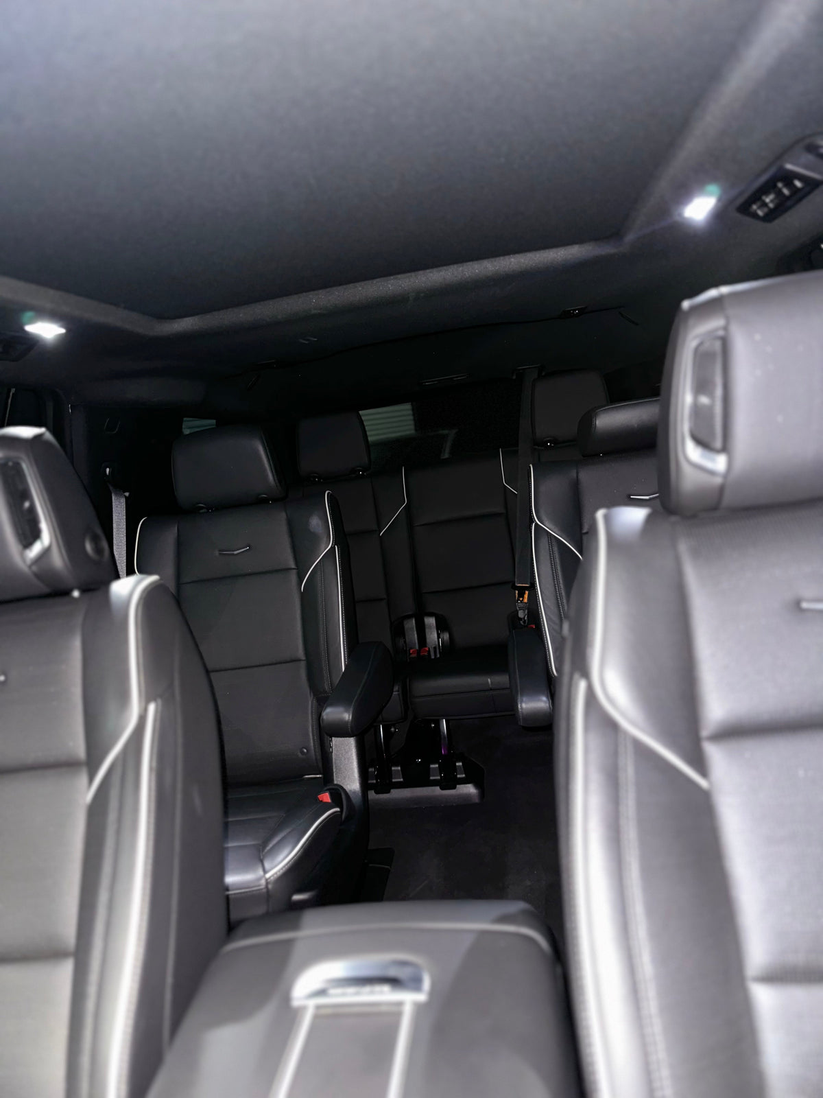 Interior view of spacious black leather SUV seats with armrests and white stitching detail, featuring multi-row seating and modern LED cabin lighting.