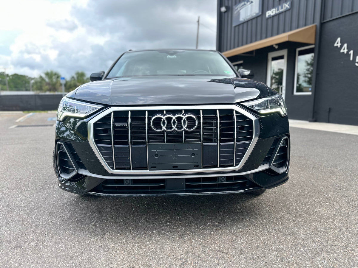 Front view of black Audi SUV with LED headlights and signature grille parked outside dealership, luxury car for sale.